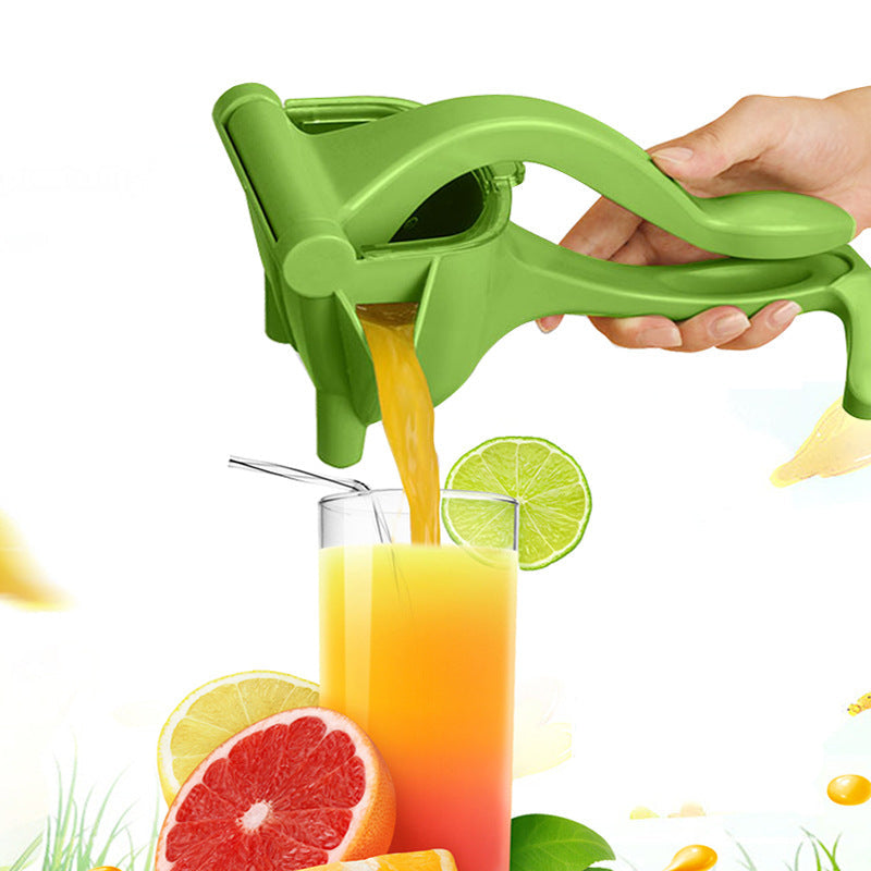 Green manual juicer squeezing orange juice into a glass with fruits and vegetables in the background.
