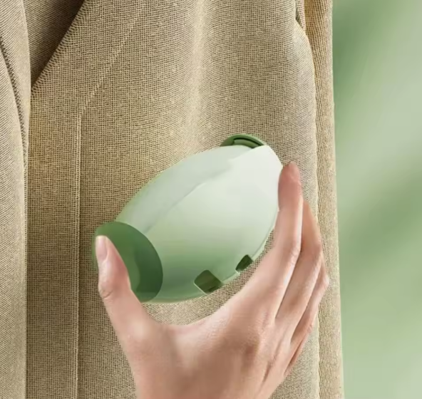 Hand holding a green portable pet hair roller against a textured beige fabric and green background